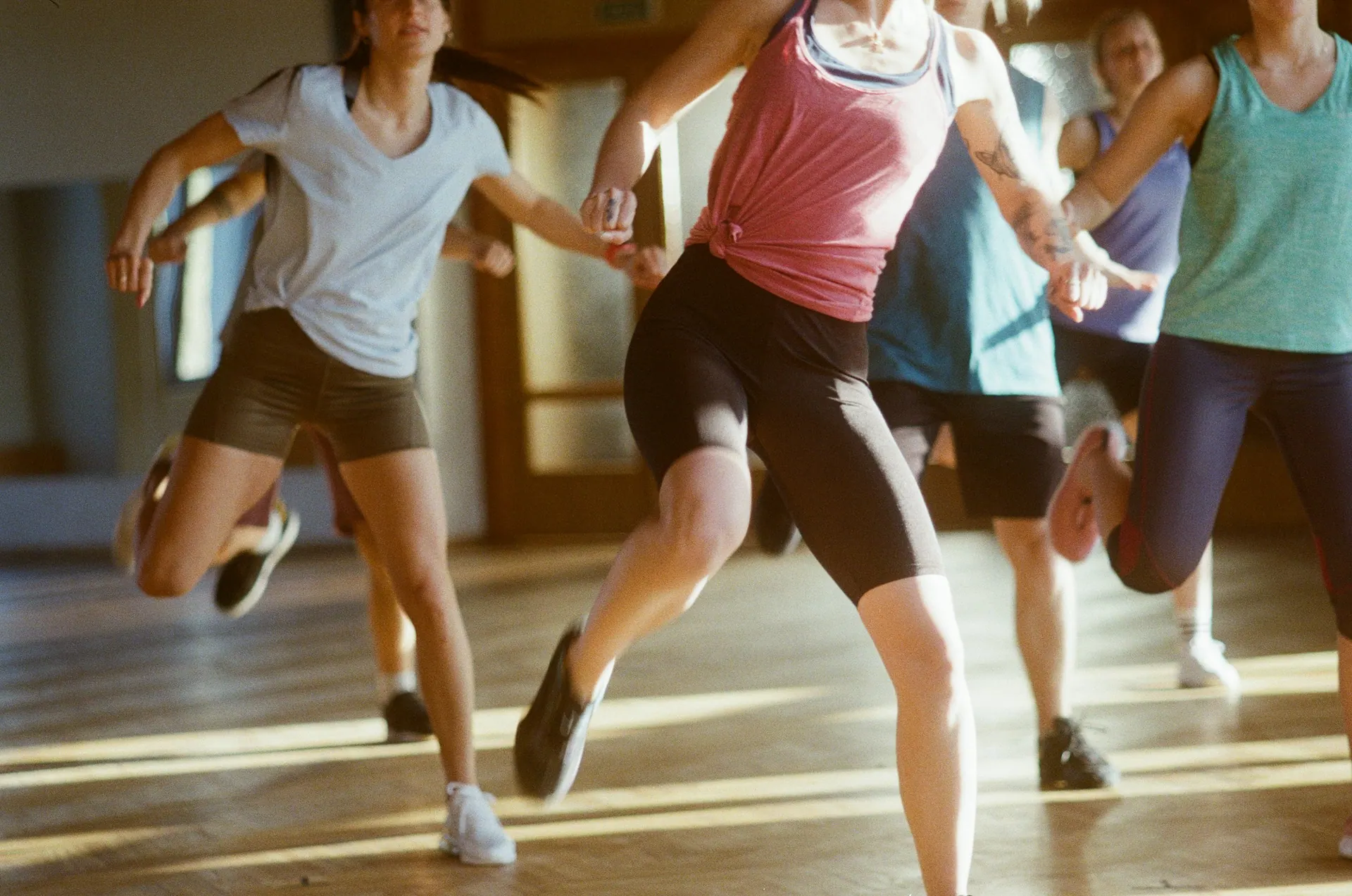 A small group mid-movement across a warm wooden studio floor