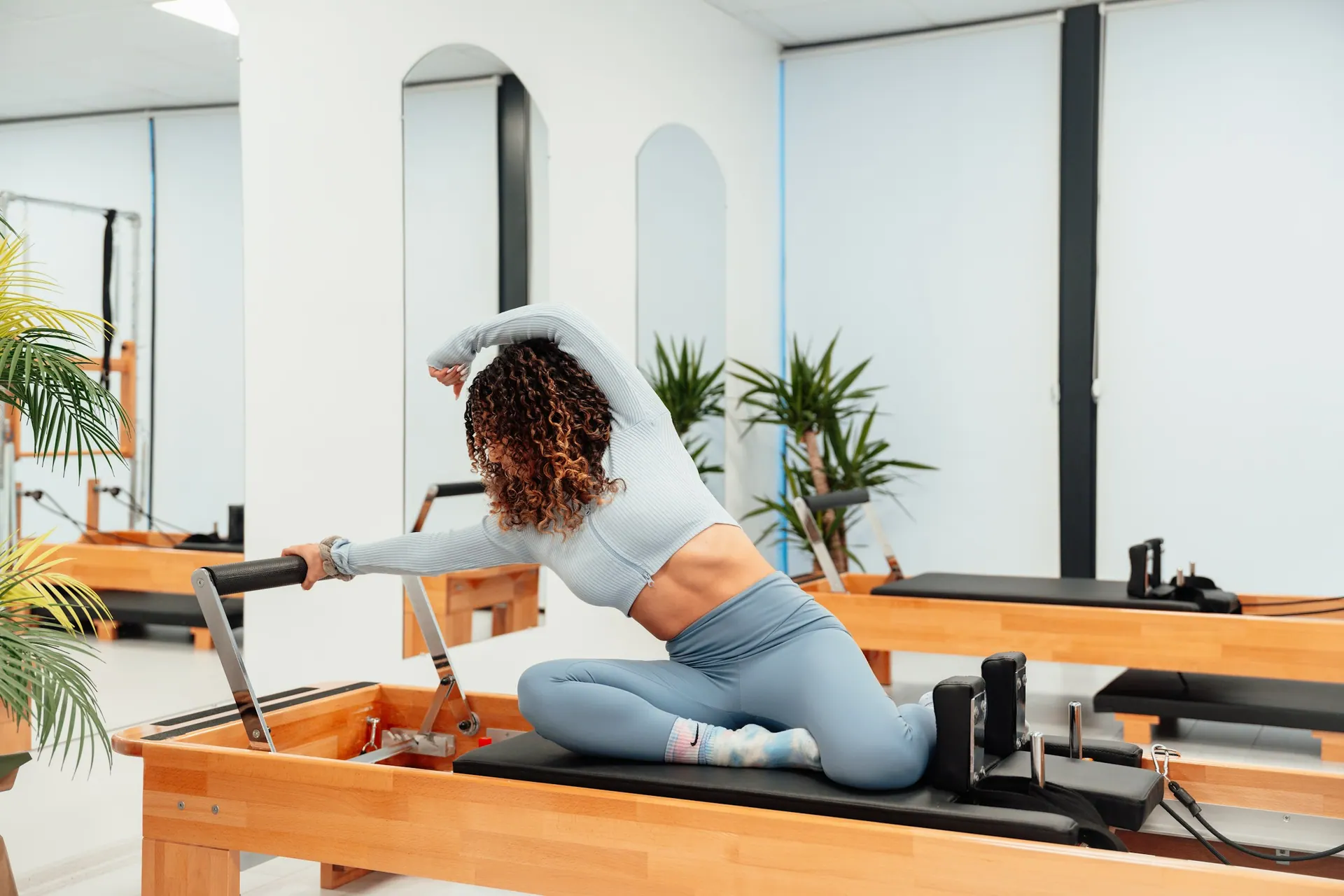 A reformer pilates side stretch in a bright studio with warm wooden equipment
