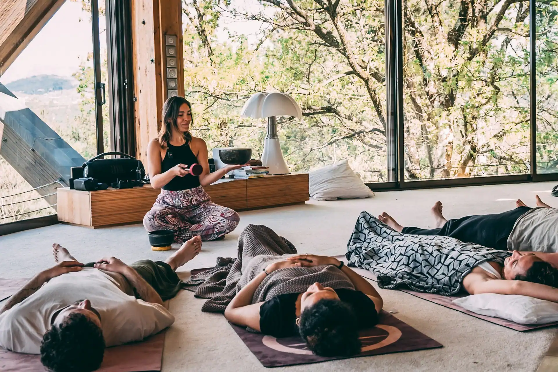 An instructor leading a sound bath in a glass-walled cabin as participants lie on mats